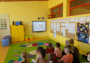 Grupa dzieci ogląda prezentację multimedialną na temat wiosennych kwiatów.